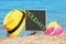 Little blackboard with word HOLIDAYS, hat and flip flops on sand