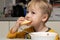 Little blond boy 3 years old is eating soup and bread in the kitchen at the table and smiling contented close-up