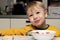 Little blond boy 3 years old is eating soup in the kitchen at the table and smiling contented close-up
