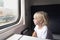 Little blond boy looks thoughtfully out the train window. Rail travel with children