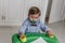 A little blond boy with a pacifier and dressed in blue, plays on a small desk