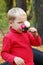 Little blond boy in red sniffs flowers