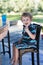 Little blond boy sitting on high chair in cafe with cocktail