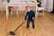 Little blond boy sweeping the floor in the kitchen. Pretty boy 3 yers old helps parents with housework.