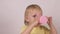 Little blond caucasian girl drinks some water from a pink mug and looks into the camera, white background, close-up