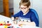 Little blond child with eye glasses playing with lots of colorful plastic blocks. Adorable school kid boy having fun