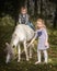 Little blond girl leading pony by bridle with her younger brother