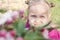 Little blond girl looks at the camera from behind the branches of a flowering tree