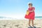 Little blond girl in red dress on the beach