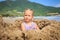 Little Blond Girl Sits in Sand Hole Plays Smiles