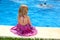 Little blond girl sitting rear back swimming pool