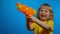 Little blond girl in yellow t-shirt with orange water gun is laughing in studio