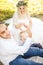 Little blond haired blue eyed toddler boy lying on wedding dress of his mother. Groom making heart shaped arm gesture