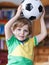 Little blond preschool boy of 4 years with football looking soccer world cup on tv.