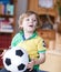 Little blond preschool boy of 4 years with football looking soccer world cup on tv.