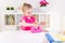 Little blonde baby girl housewife playing with toy pink iron. Ironong clothes on a white table. Housework, helper