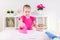 Little blonde baby girl housewife playing with toy pink iron. Ironong clothes on a white table. Housework, helper