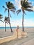 Little blonde Caucasian girl sitting relaxing dreaming on empty Hollywood ocean beach in Florida. Child among tall palm trees on