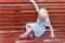 Little blonde girl in blue dress sits on red bench. Child is playing on brown bench outdoors