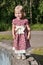 Little blonde girl in dress stands in park at sunny day a