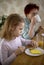 A little blonde girl is having breakfast in the kitchen with her beloved grandmother. The child eats a healthy breakfast