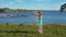 Little blonde girl inflates large soap bubbles against backdrop of sea coast.