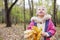 Little blonde girl with maple leaflets looks up.