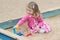 Little blonde girl playing in sandbox with plastic toy tools