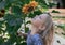 Little blonde girl raised her head and sniffs a sunflower,