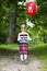 Little blonde girl with red balloon walking on footpath.