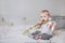 Little blonde girl sitting on a bed with pink flowers and a ribbon and biting them, portrait of a cute baby on a light background