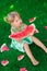 Little blonde girl sitting on the grass around a slices of watermelon in summer. Serious.