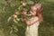 Little blonde girl stands near an apple tree