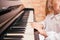Little blonde girl in white trying to play on dark vintage piano, closeup