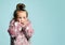 Little blonde kid with bun hairstyle, dressed in pink faux fur coat. She looking wondered, posing on blue background. Close up