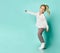 Little blonde kid in shirt with hearts print, checkered pants, white sneakers. Smiling, dancing on blue background. Full length