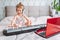 Little blonde toddler girl play classic digital piano at home during online lesson with laptop. Online education concept