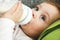 Little blue-eyed girl drinks milk from a bottle lying on the bed