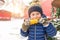 Little boy 2-3 years in a blue jacket and hat. The child in winter on the street eats boiled corn from a stick. Concept