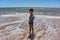 Little boy on anjuna beach with yellow sand, blue ocean and waves. North Goa, India. March 12, 2020.