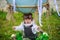 A little boy in a aviator`s hat sits in a basket of a toy balloon in a field