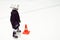 A little boy in black hockey uniform and a white helmet on skates next to an orange cone on white ice on the ice hockey