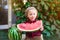 A little boy with blond hair n the summer on a sunny day sitting at a gazebo with a green grapes and eating a watermelon