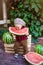 A little boy with blond hair n the summer on a sunny day sitting at a gazebo with a green grapes and eating a watermelon