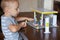 Little boy with blond hair and plastic gas station set on a wooden table, with a small car model.