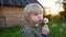 Little boy blows down dandelion fluff. Making a wish. Kids`s fun in the summer outdoors. Summer activity for child.