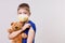 Little boy in blue t-shirt and mask with bear toy shows his shoulder after vaccination. Children hand with Adhesive plaster