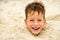 Little boy buried in the sand on beach