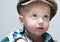 Little boy in a cap sits at the table, he is dressed in a shirt box , it stylish hat and he looks up