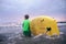 Little boy carries yellow surf board into ocean waves. Surfing First steps concept